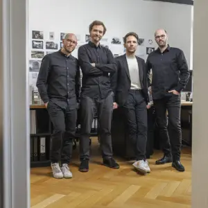 Vier männliche Architekten in dunkler Kleidung stehen souverän in einem hellen Büro – professionelles Teamfoto für ein Architekturbüro in Ulm.