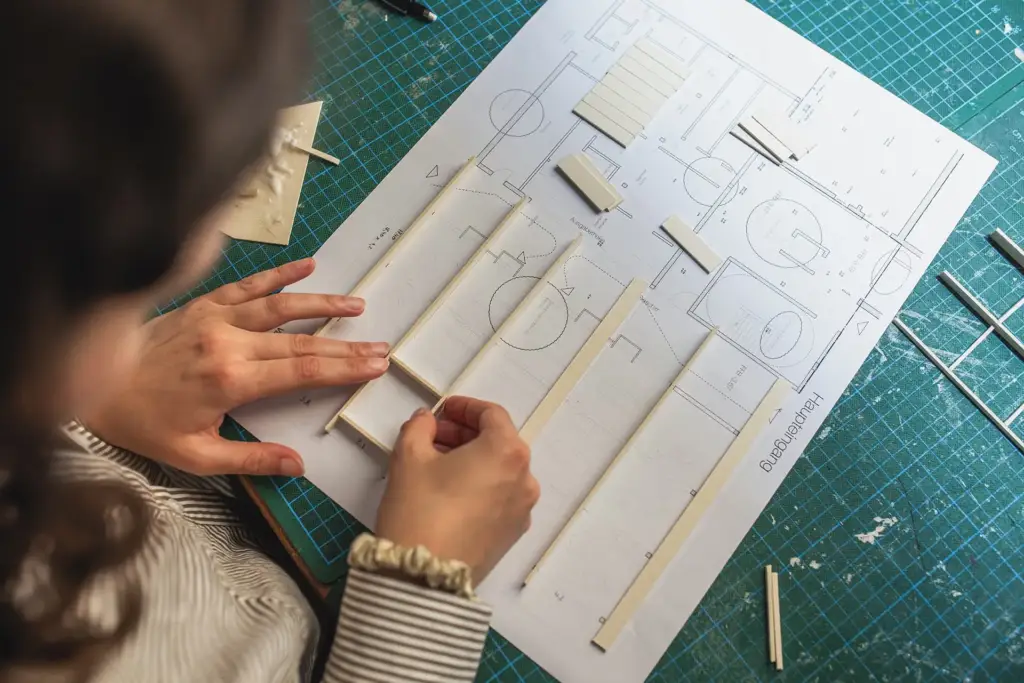 Draufsicht auf Hände, die filigrane Elemente an einem Architekturmodell aus Holz in Ulm platzieren.