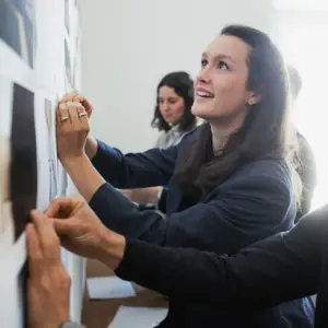 Eine junge Frau im Blazer arbeitet lächelnd mit Kollegen an einer Entwurfswand in einem hellen Büro – authentische Businessfotografie aus Ulm.