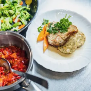 Ein ansprechend angerichteter Teller mit Braten, Serviettenknödeln und Gemüse in einer Gastro-Küche – professionelle Food-Fotografie aus Ulm.