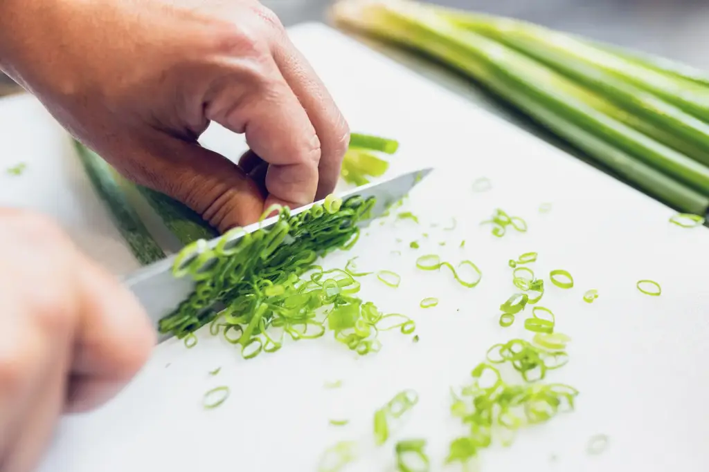 Nahaufnahme der Hände eines Mitarbeiters beim präzisen Schneiden von Frühlingszwiebeln in einer Ulmer Gastronomie-Küche.