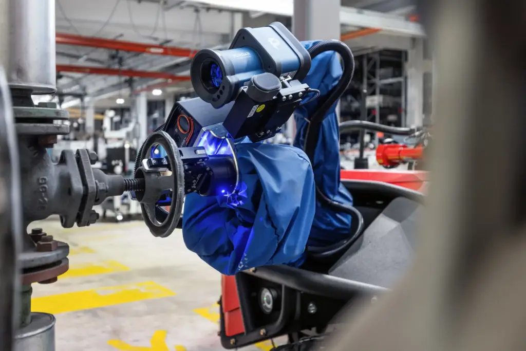 Nahaufnahme eines blauen Roboterarms mit Sensorik und Kameraeinheit, der ein Handrad an einer Industriearmatur bedient – Industriefotografie aus Ulm.