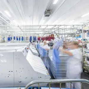 Innenansicht einer hellen, modernen Industriewäscherei in Ulm mit automatisierten Anlagen und Mitarbeitern bei der Textilpflege.