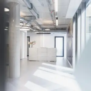 Ein heller, moderner Empfangsbereich eines Büros in Ulm mit Sichtbeton-Säule, minimalistischem Tresen und industriellem Decken-Design.