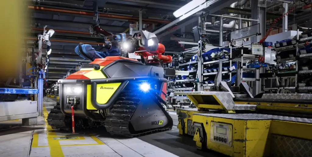Der ferngesteuerte Löschroboter Magirus Wolf R1 mit eingeschalteten LED-Scheinwerfern manövriert durch eine enge Industriehalle mit gelben Markierungen und Logistik-Equipment – Industriefotografie aus Ulm.