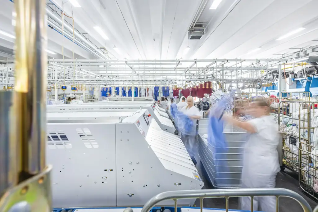 Blick in eine lichtdurchflutete Produktionshalle in Ulm mit Mitarbeitern und hochmodernen Textilmaschinen.