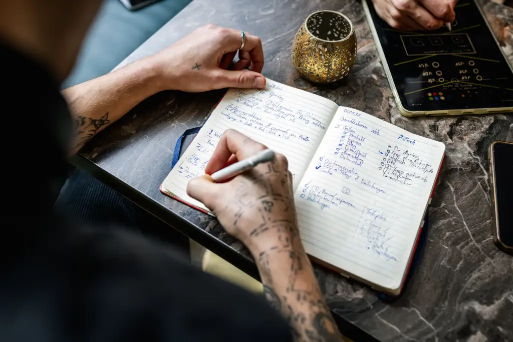 Nahaufnahme von Händen, die handschriftliche Notizen und Checklisten in ein Notizbuch während einer Startup-Planung in Ulm schreiben.