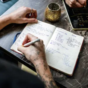 Nahaufnahme von Händen, die handschriftliche Notizen und Checklisten in ein Notizbuch während einer Startup-Planung in Ulm schreiben.