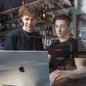 Zwei junge Gründer arbeiten gemeinsam an einem Laptop in einem modernen Ulmer Café.